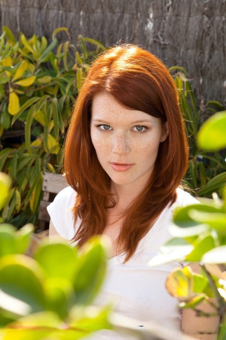 Natural redhead Mia Sollis casually strips naked on a patio bench