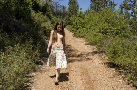 Young looking solo girl gets naked while walking a road through the woods