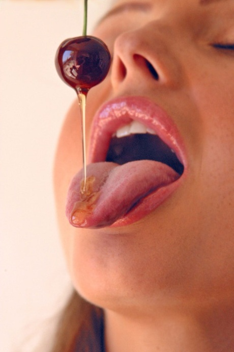 Pretty girl Sandra Shine curls her tongue while sucking juice from a cherry
