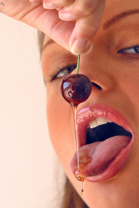 Pretty girl Sandra Shine curls her tongue while sucking juice from a cherry