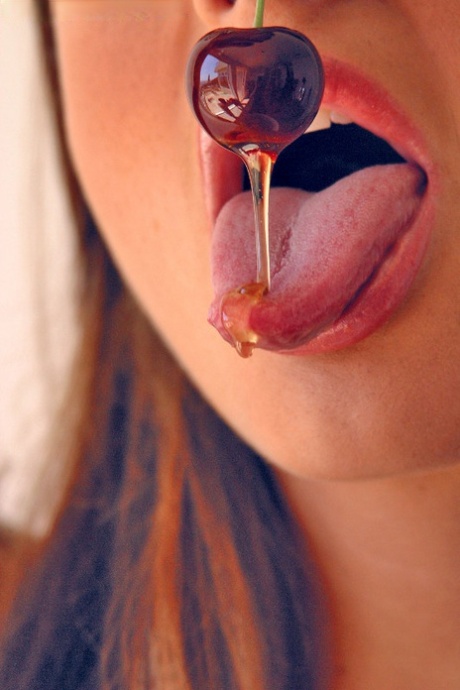 Pretty girl Sandra Shine curls her tongue while sucking juice from a cherry