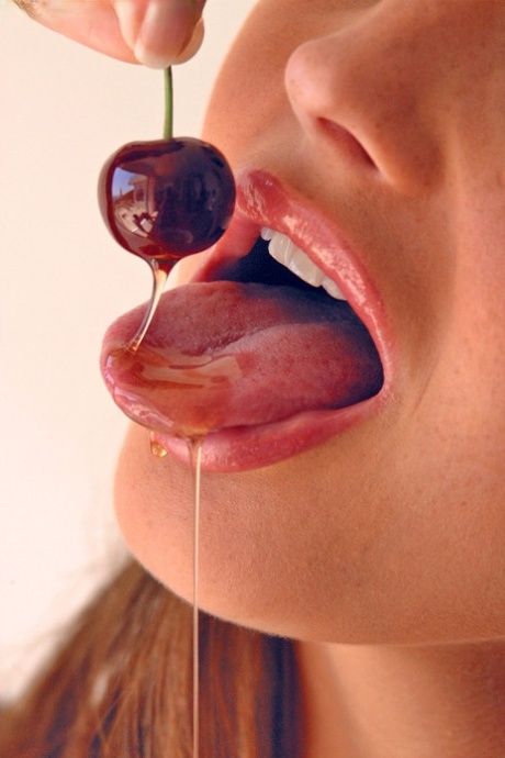 Pretty girl Sandra Shine curls her tongue while sucking juice from a cherry