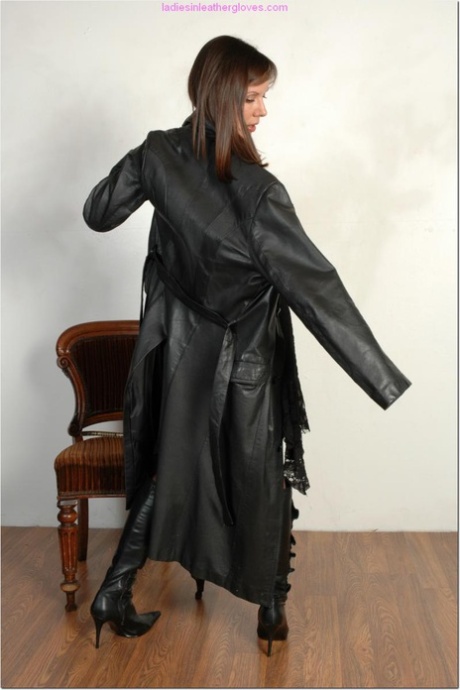 Brunette female dons long leather coat in leather boots and stockings